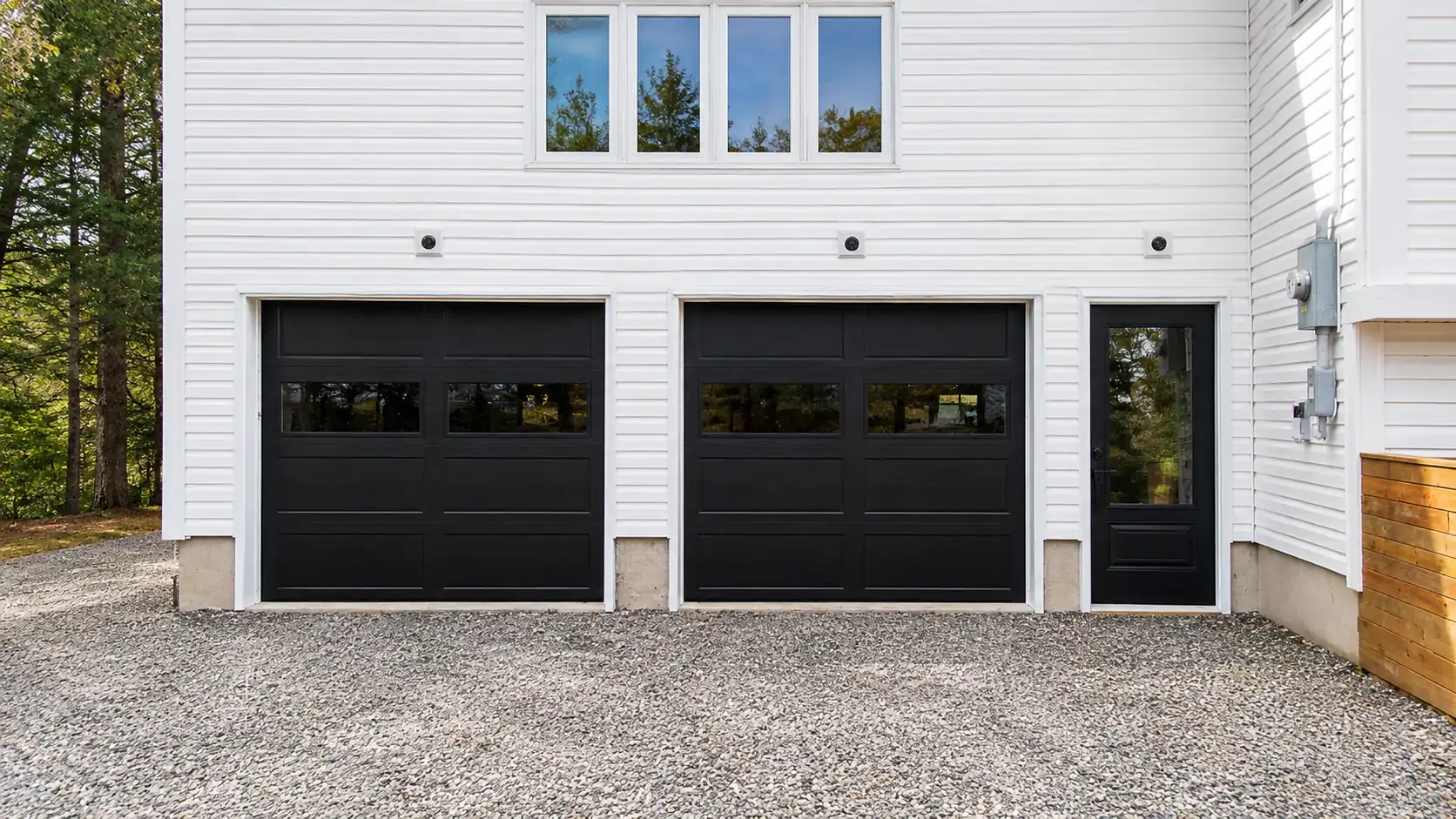 Completed window and door installation in Comox Valley — black garage doors entry door and upper windows on finished white exterior